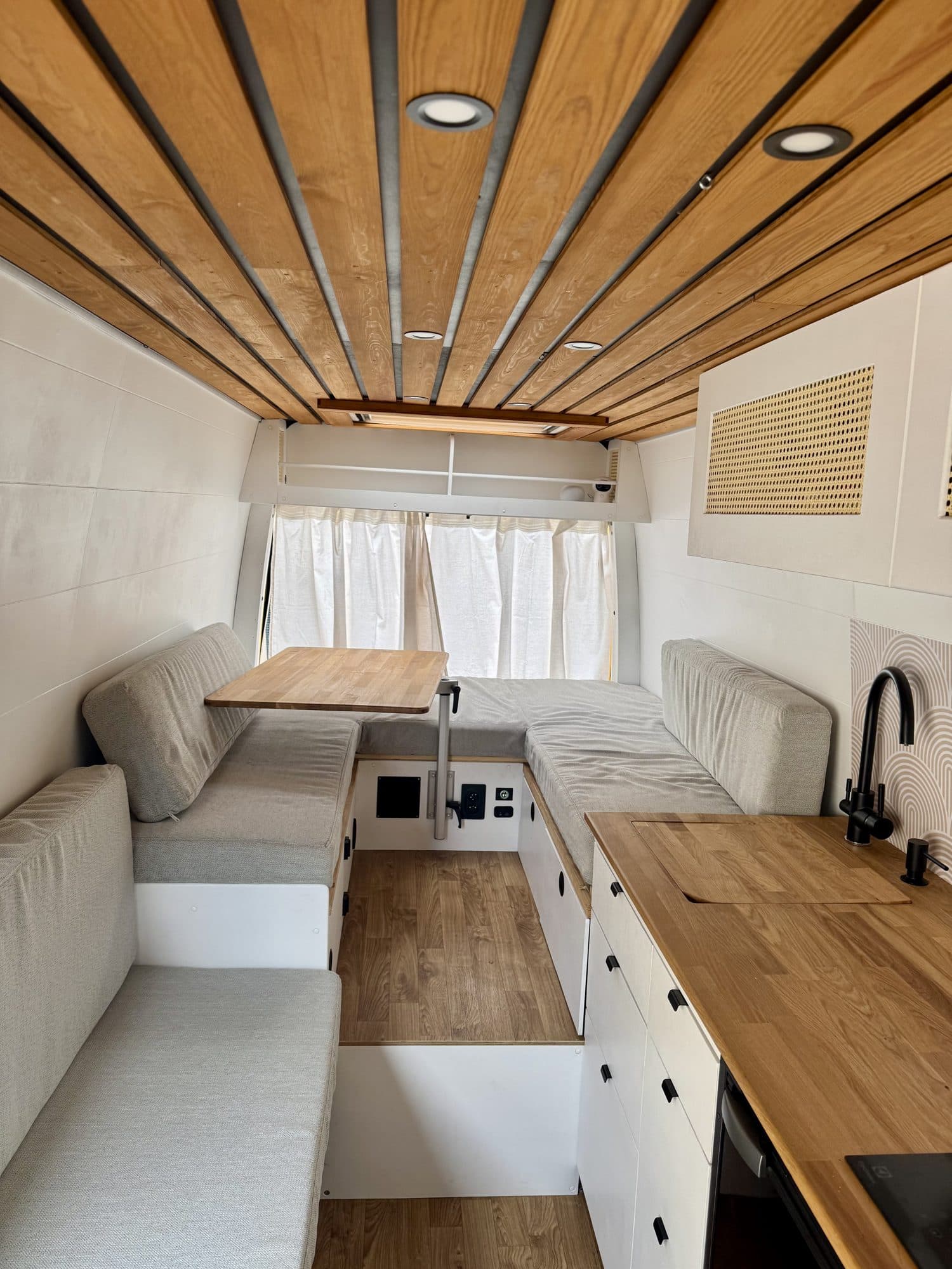 Inside Žluťák: wooden slat ceiling, grey bench seating around a table and a wooden kitchen counter